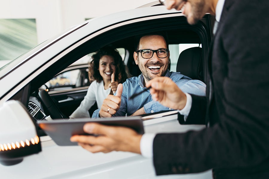 A happy couple talking to a car salesman wanting to test drive a car